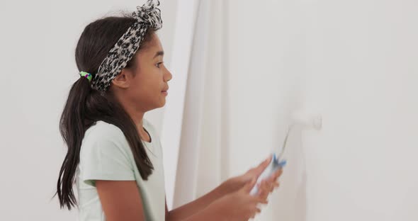 Happy Little Girl in Her Hands Holding a Roller with White Paint Carefully Trying to Paint the Walls