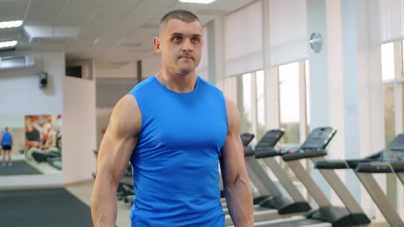 A Young Handsome Coach with a Muscular Body Poses in Gym