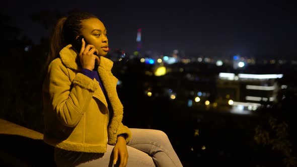 A Young Black Woman Gets a Call and Talks on a Smartphone with a Smile at Night