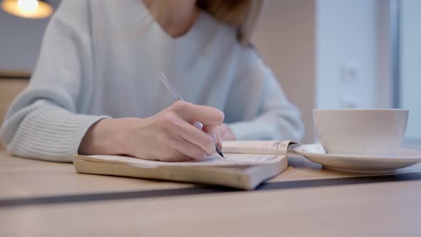 Unrecognizable Young Woman Writing with Pen in Workbook