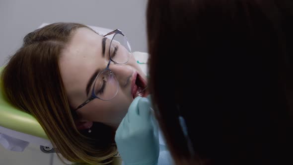 Female Dentist Examines with Dental Tools Teeth Features of Patient with Glasses