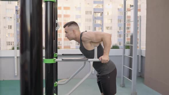 Young Man Workout Out Arms on Dips Horizontal Bars Training Triceps and Biceps Doing Push Ups