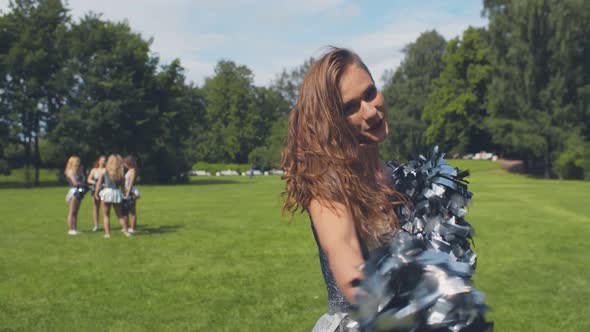 Portrait of Young Smiling Cheerleader Shaking Pompons and Posing at Camera