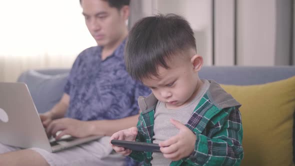 Boring Boy Using Smartphone While Father Working On Laptop