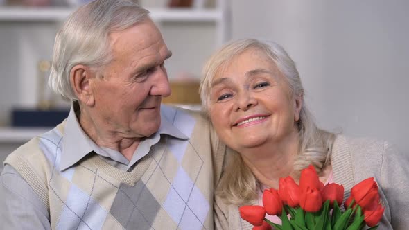 Smiling Aged Couple Embracing, Woman Smelling Flowers, Celebrating Anniversary