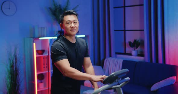 Asian Guy in Training Clothes Walking on Treadmill and Showing Thumbs Up Into Camera