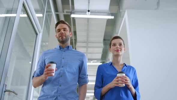 Colleagues Walking with Paper Cups in Office