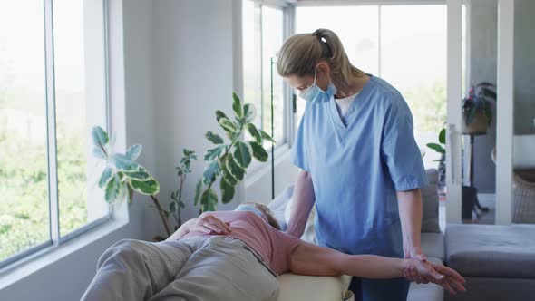 Female health worker stretching arm of senior woman at home