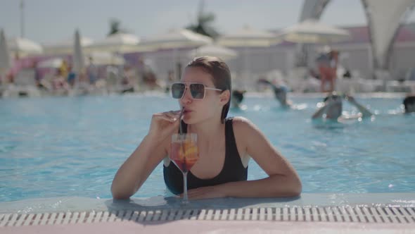 Miss with Sunglasses Drinks a Cocktail While in the Pool