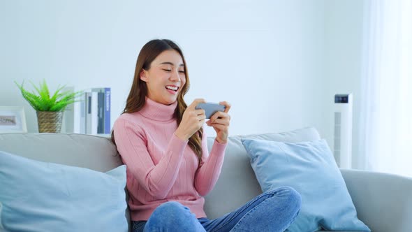 Asian young beautiful woman playing mobile game on smartphone at home feel happy and relax.