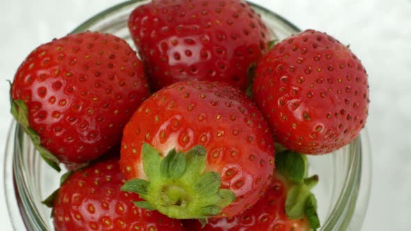 Glass jar with red ripe strawberries rotating on a white background. Ripe summer red strawberry