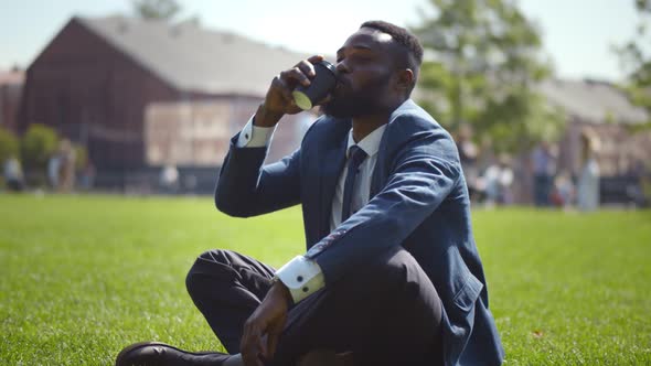 Young African Man Sitting in Park and Looking Away Drinking Coffee