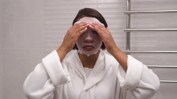 A Young Woman with Tanned Skin Uses a Cloth Mask to Moisturize Her Face