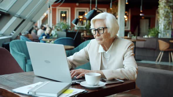 Portrait of Senior Businesswoman Working with Laptop Typing at Table in Cafe