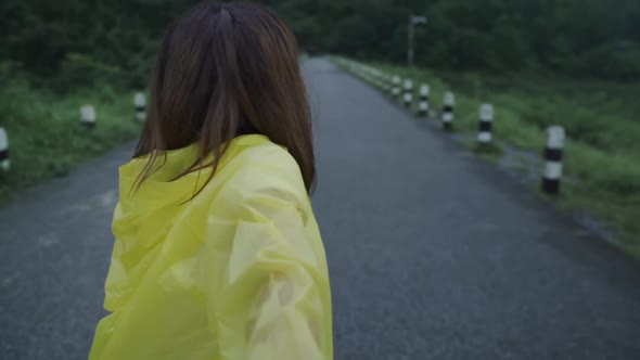 Young Asian woman feeling happy playing rain while wearing raincoat standing near lake.