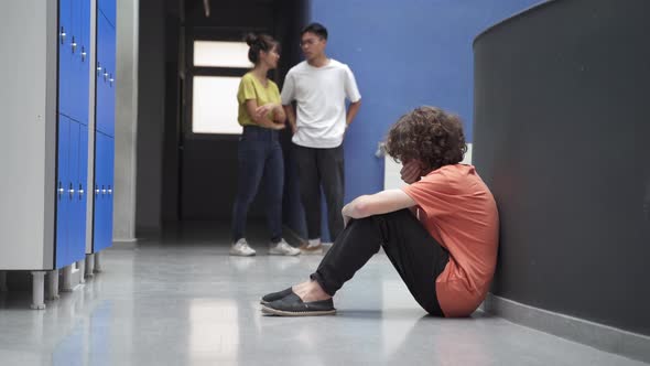 Sad Teenager Sitting Alone on Floor Victim of Bullying While Classmates Ignore Him