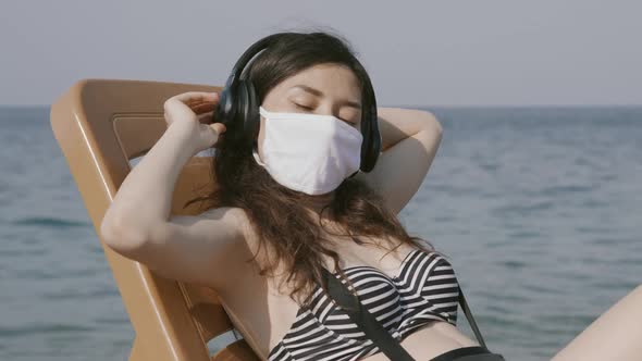 Young Woman in Medical Mask Relaxing on Beach Deck Chair By the Sea with Eyes Closed Wearing