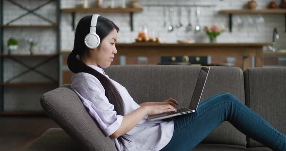 Asian Woman in Headphones Working with Laptop Computer Looking at Screen Typing Message Resting on