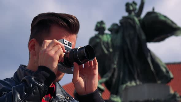 A Young Handsome Man Takes Photos with a Camera - Closeup From Below - a Statue in the Background