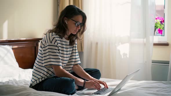 Young Woman Freelancer Working on a Laptop While Sitting on a Bed