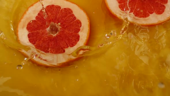 Grapefruit slices fall into the water on an orange background. Slow motion.