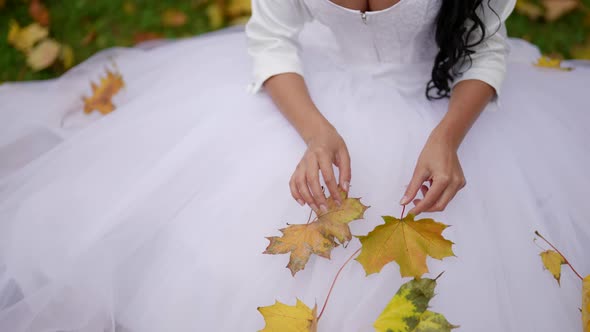 Bride in Autumn Beautiful Woman in Wedding Dress is Sitting on Ground in Park in Fall Day