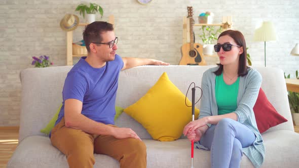 Young Man Communicates with a Blind Woman with a Disability Sitting on the Couch