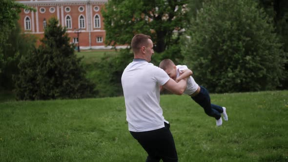 Father Has Fun with His Child Circling His Son in Nature Standing on a Green Field in Summer