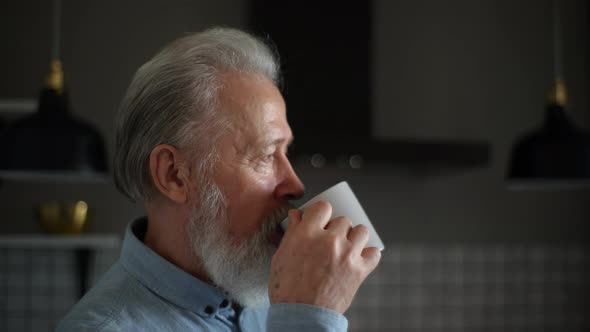 Closeup Face of Pensive Bearded Senior Older Man with Grey Hair Drinking Tea at Home Kitchen Having