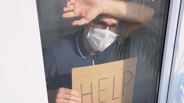 Young frightened man wearing a white face mask, stand behind glass window, pressed the glass inside