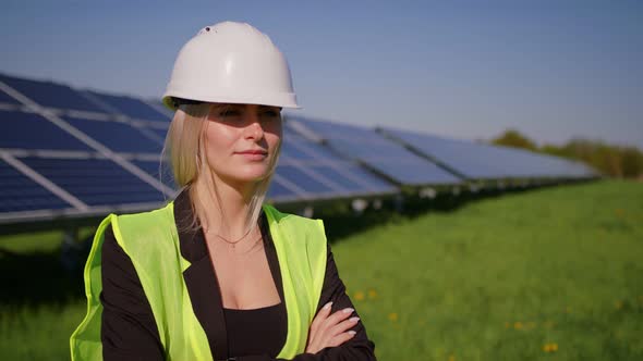 Portrait of Beautiful Female Engineer Technologist Standing Among Solar Panels with Her Arms Crossed