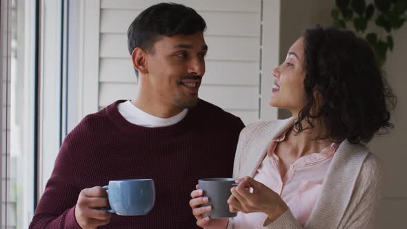 Romantic hispanic couple embracing standing in window having coffee