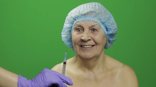 Smiling Elderly Female Lady in Protective Hat Scared of Syringe with Medicines