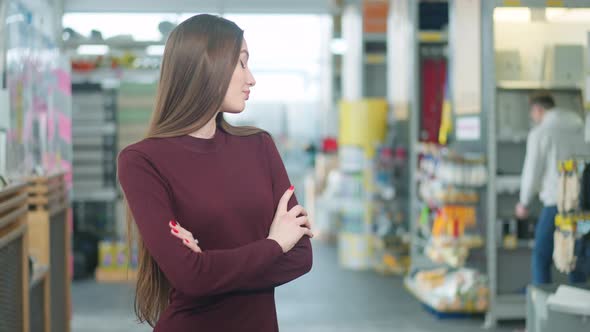 Bored Young Beautiful Caucasian Woman Looking Back at Absorbed Man Choosing Supplies in Hardware