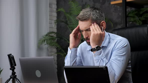Tired man trader rubs head, acute headache, migraine after hard work at laptop