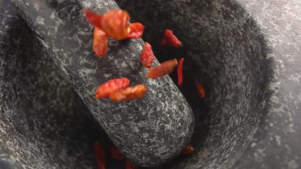 Closeup of Red Cayenne Pepper Pods Falling and Bouncing in the Stone Mortar