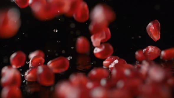 Pomegranate seeds falling on water surface. Slow Motion.