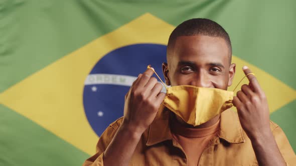 Happy Black Man Removing Mask and Smiling against Brazilian Flag