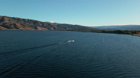 Motorboat crossing wide blue Clutha river in New Zealand. Low dolly aerial view of boat speeding acr