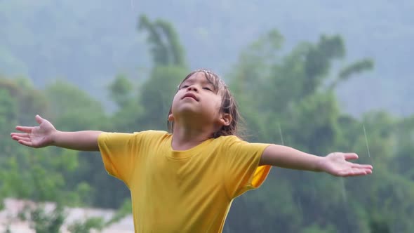 Cute little girl having fun catching rain drops. Kids play in summer rain. Child playing outdoor.