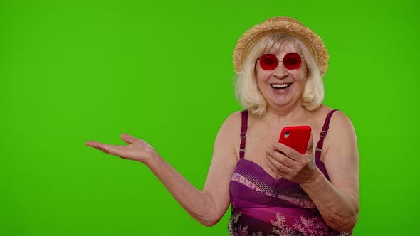 Senior Pensioner Woman Tourist in Swimsuit Points Hand Shows Advertising Content From Mobile Phone