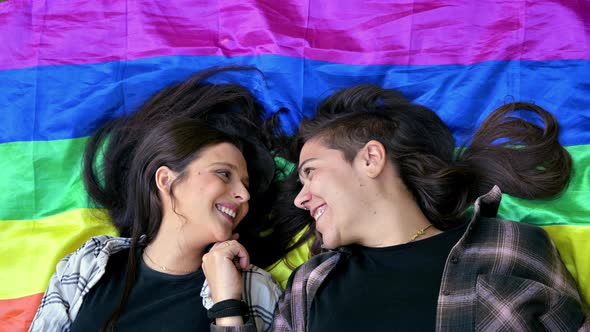 Lesbian Couple Wearing a Lgbt Rainbow Flag and Kissing Lying on the Floor