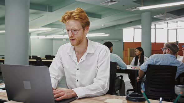 Employee Working at Laptop on Business Project Sitting at Table in Office Leaning Back in Chair