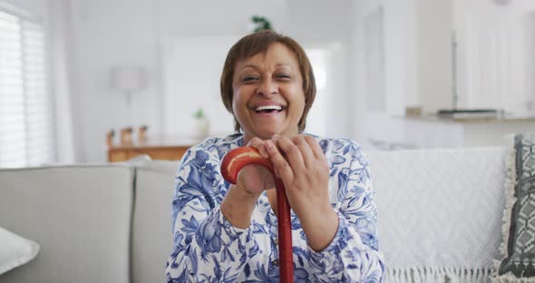 Portrait of happy african american senior woman sitting leaning on walking stick, smiling