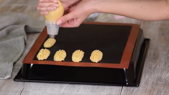 Pastry Chef with Confectionery Bag Squeezing Fresh Pastry Dough on Tray with Paper