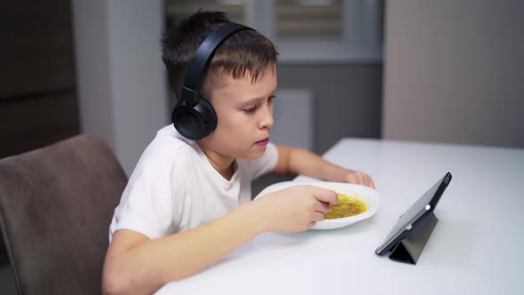 Boy eating at home. Adorable boy eating while watching movie on tablet