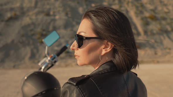 Portrait of confident woman in leather jacket sitting on a motorcycle and posing