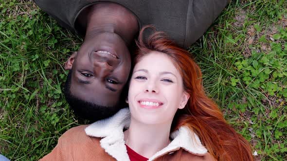 young mixed couple opening their closed eyes lying on lawn,smiling