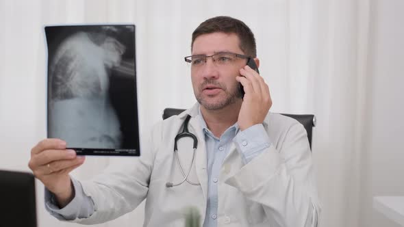 Doctor Talking On Smartphone While Looking At X-ray Film. medium shot