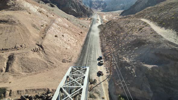 Vehicles off-roading past a creek and train truss bridge in Afton Canyon, Mojave Desert, California.